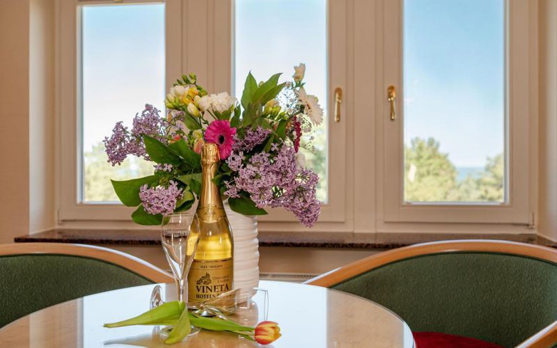 Willkommen im VINETA - Vineta Sektflasche mit Blumenstrauss und Sektglaesern