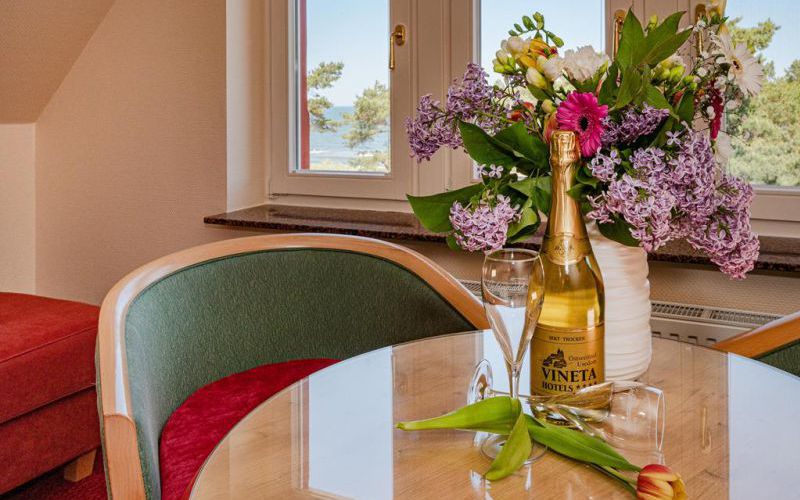 Willkommen im VINETA - Vineta Sektflasche mit Blumenstrauss und Sektglaesern und Blick aus dem Fenstzer auf die Ostsee